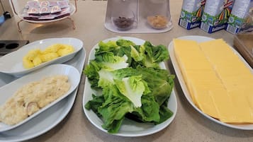 Una mesa con platos de comida, incluyendo huevos revueltos, una ensalada y un bloque de queso.