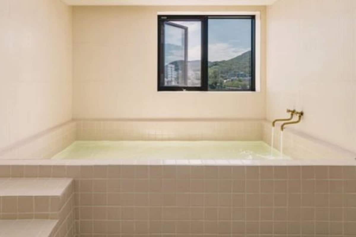 A bathroom with a bathtub, a window, and a view of a mountain.