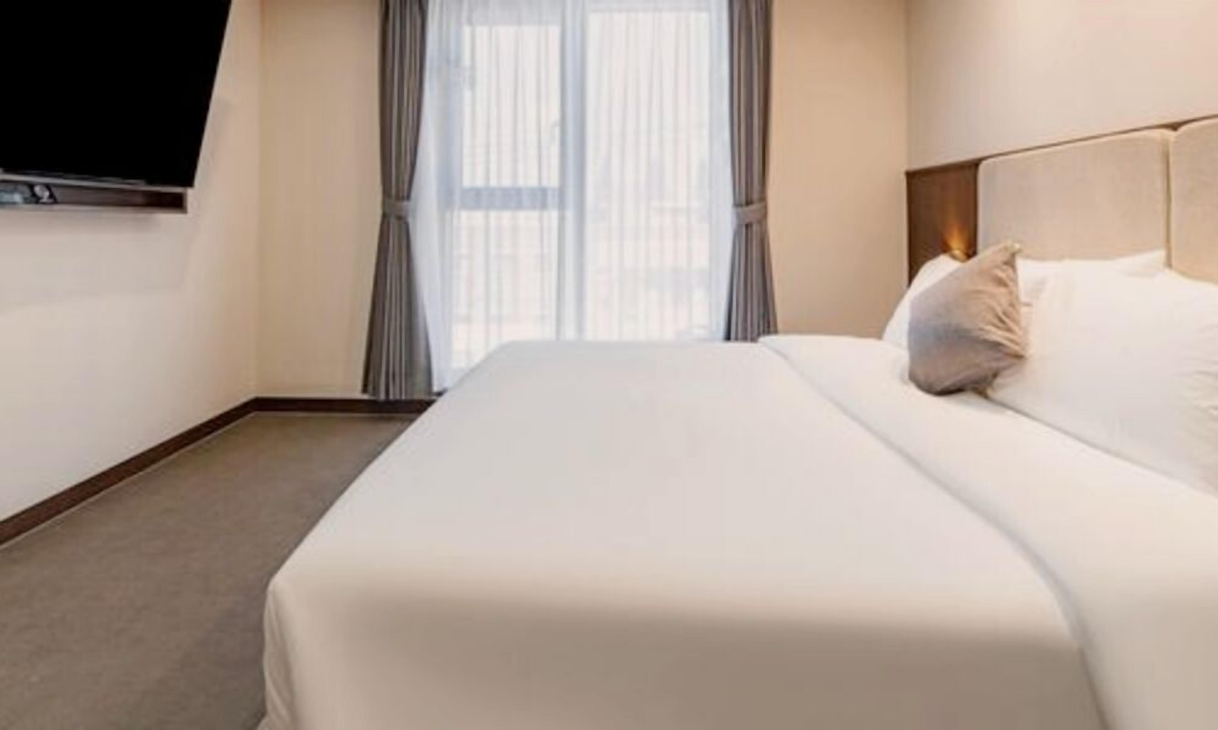 Une chambre d’hôtel avec un grand lit, une tête de lit et une fenêtre avec des rideaux.
