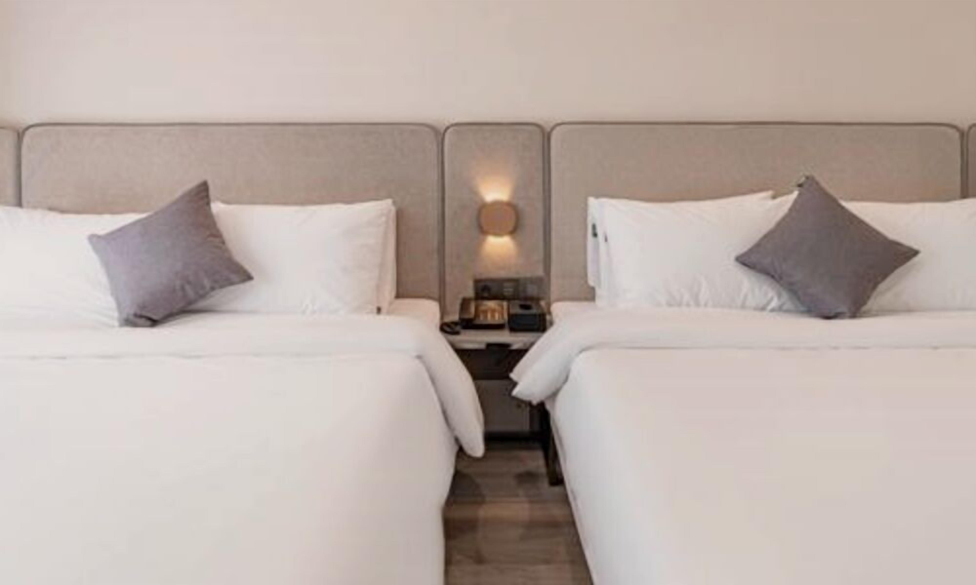 A hotel room with two single beds, each with a pillow and a nightstand.