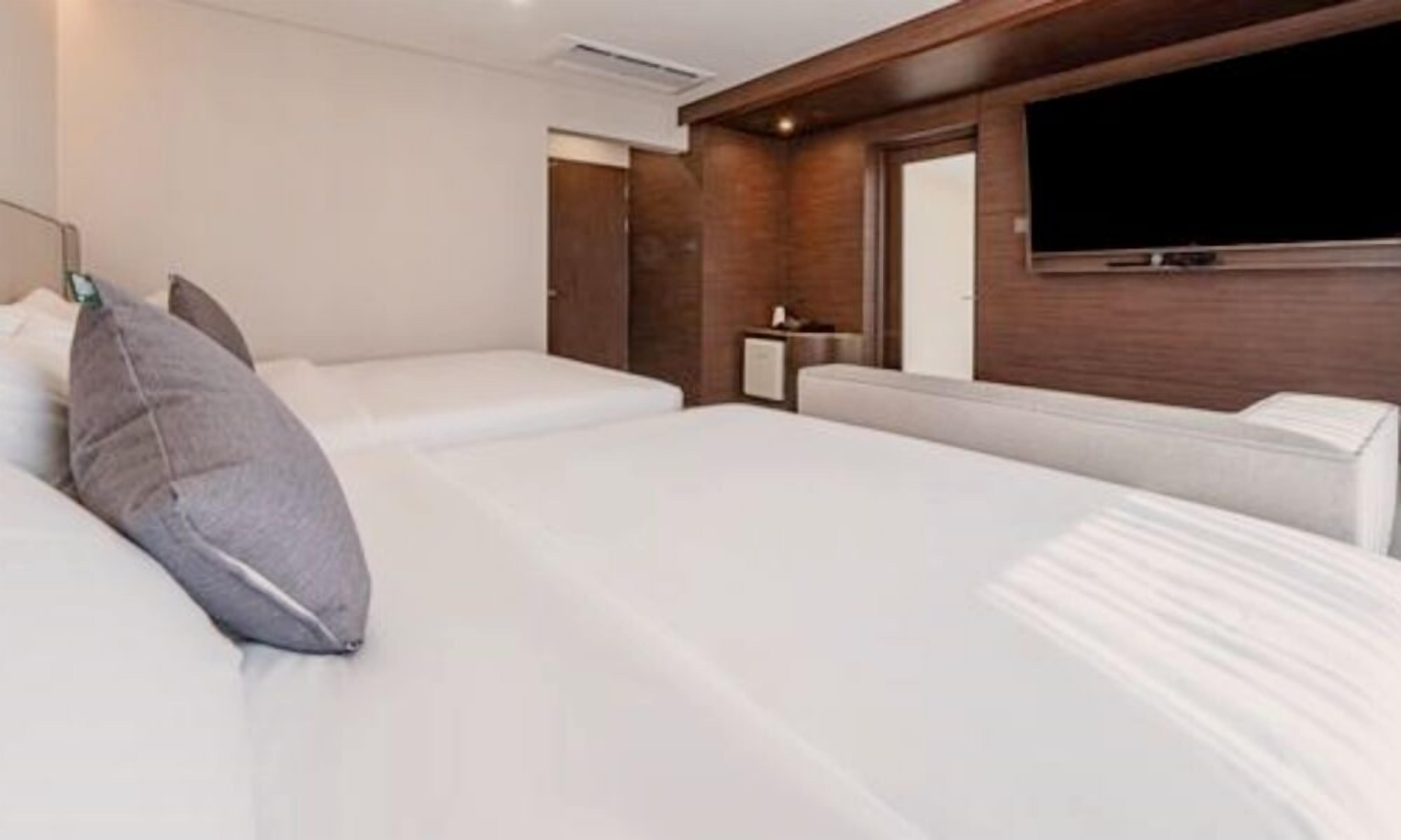 A hotel room with two beds, a flat-screen TV mounted on the wall, and a wooden accent wall.