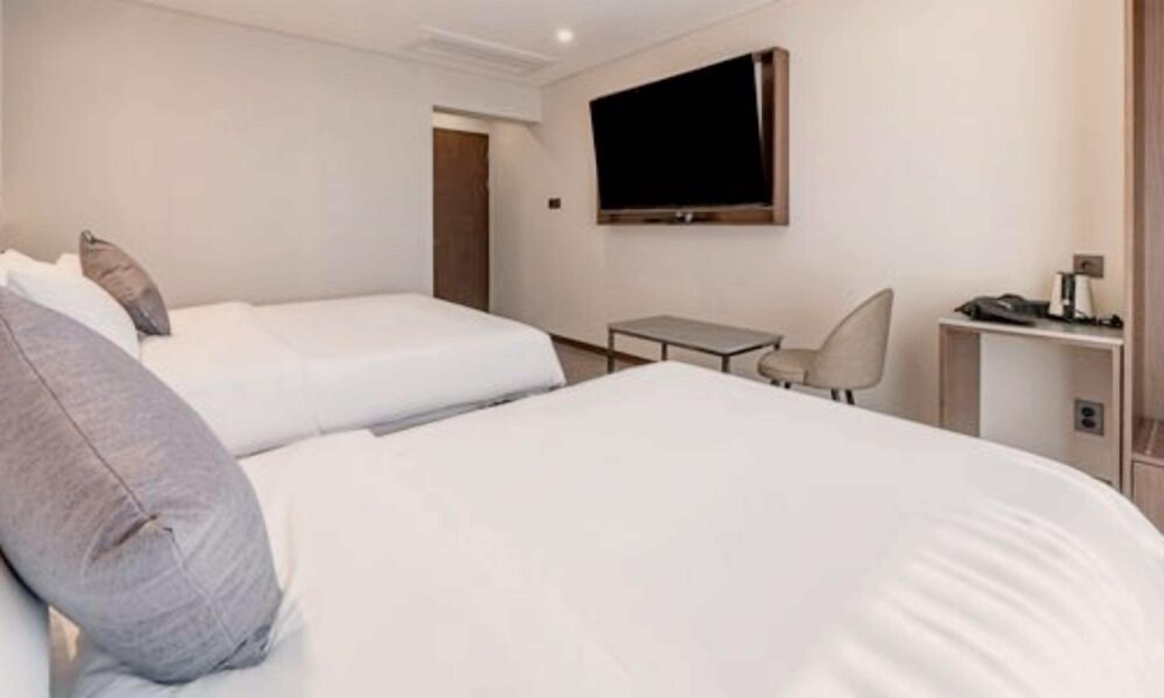 Una habitación de hotel con dos camas, televisión, escritorio y silla.