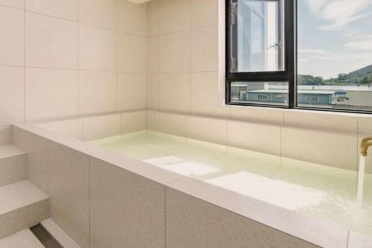 A modern bathroom with a bathtub, a window, and a view of buildings outside.