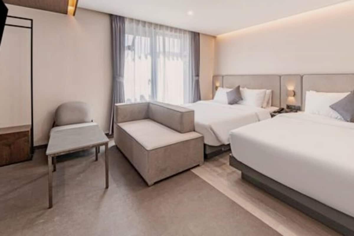 A hotel room with two beds, a sofa, a small table, and a window with curtains.
