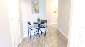 Een eetgedeelte met een ronde tafel en stoelen, een kleine potplant en twee aan de muur hangende schilderijen.
