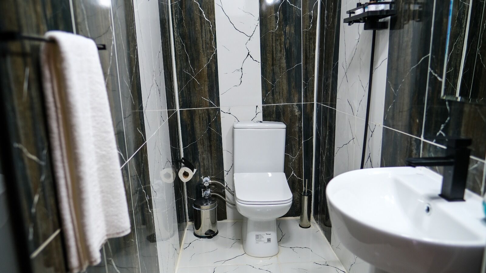 A bathroom with a toilet, sink, and marble walls.