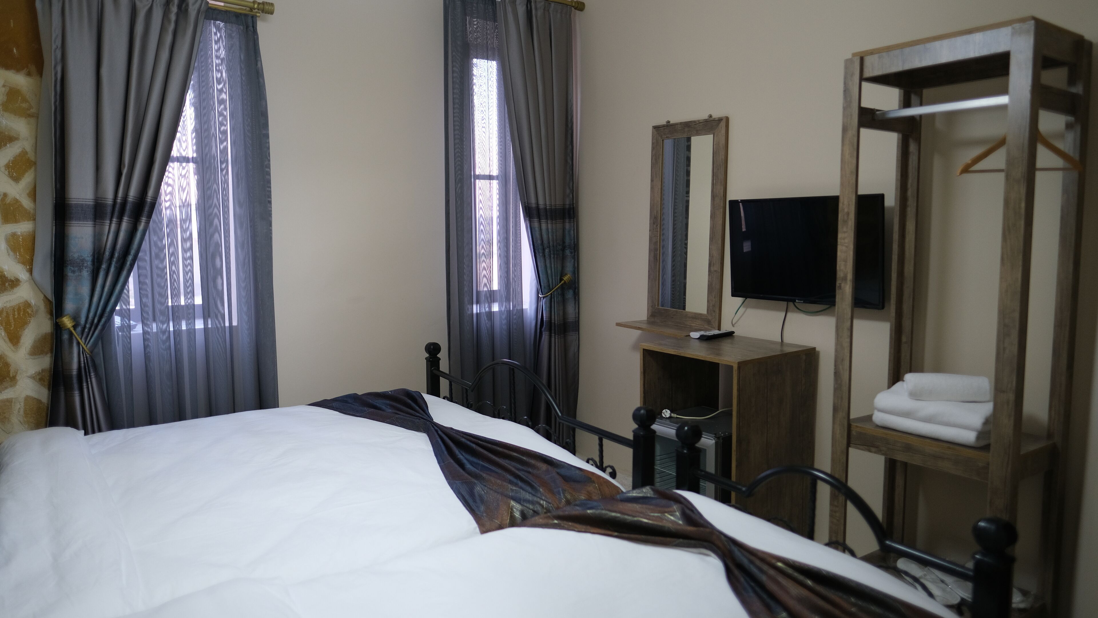 Una habitación de hotel con cama, cómoda de madera, espejo, televisor y toallero.