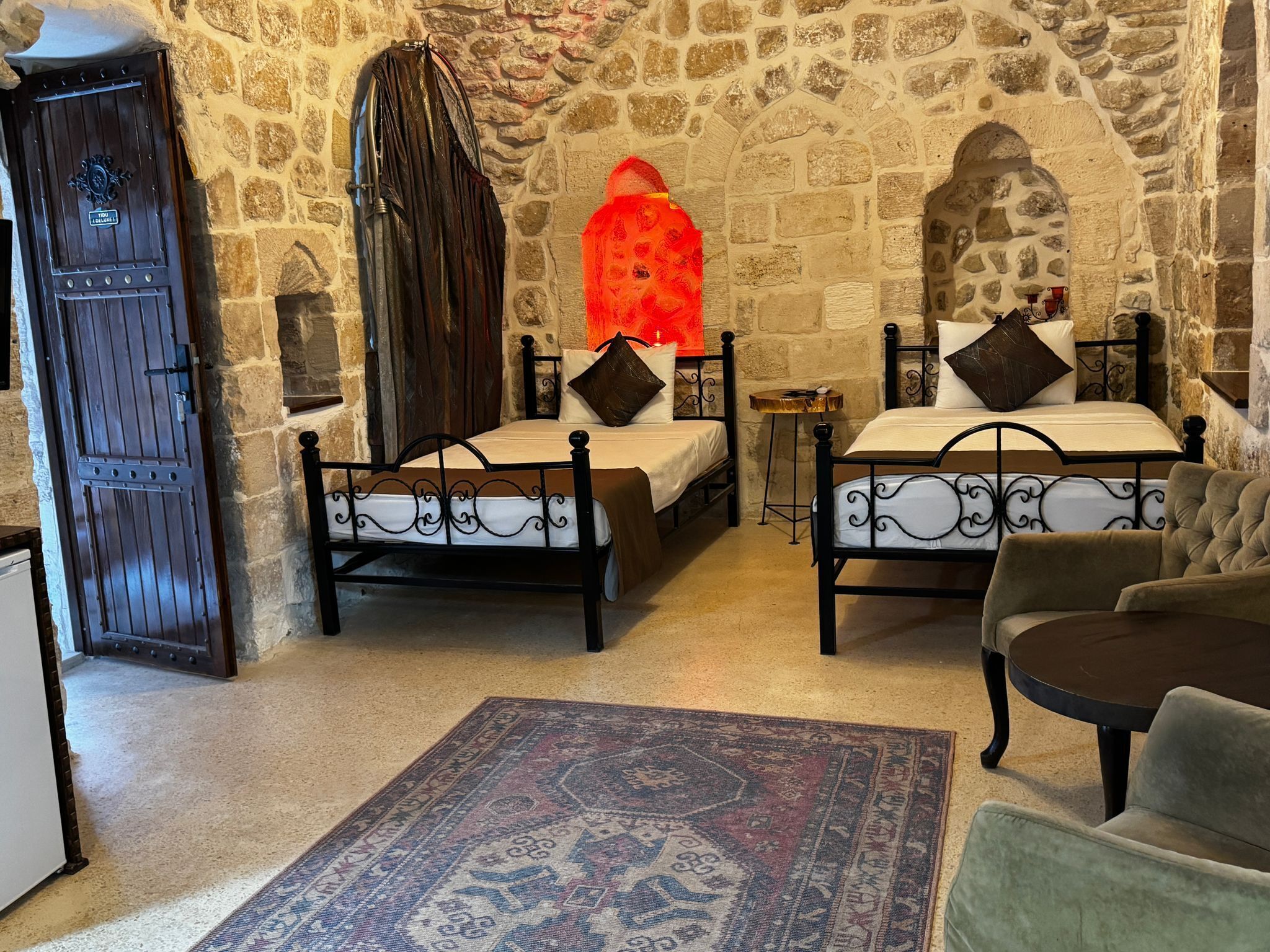 Une chambre avec deux lits, un mur en pierre, une porte en bois et un tapis à motifs.
