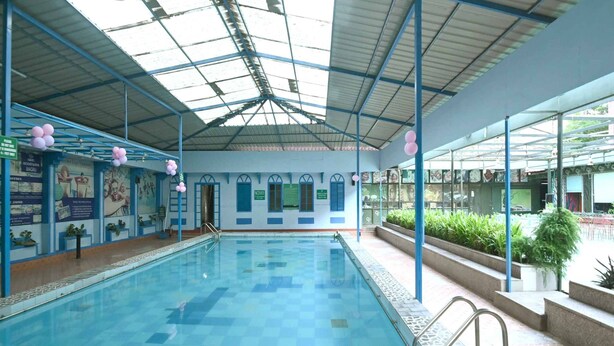 An indoor swimming pool with clear blue water, surrounded by walls with informational posters and a glass ceiling. - Golden Days Resort and Spa (Jaipur)