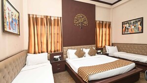 A hotel room with a large bed, two smaller beds, a nightstand, a wall-mounted tree decoration, and two paintings. - Golden Days Resort and Spa (Jaipur)