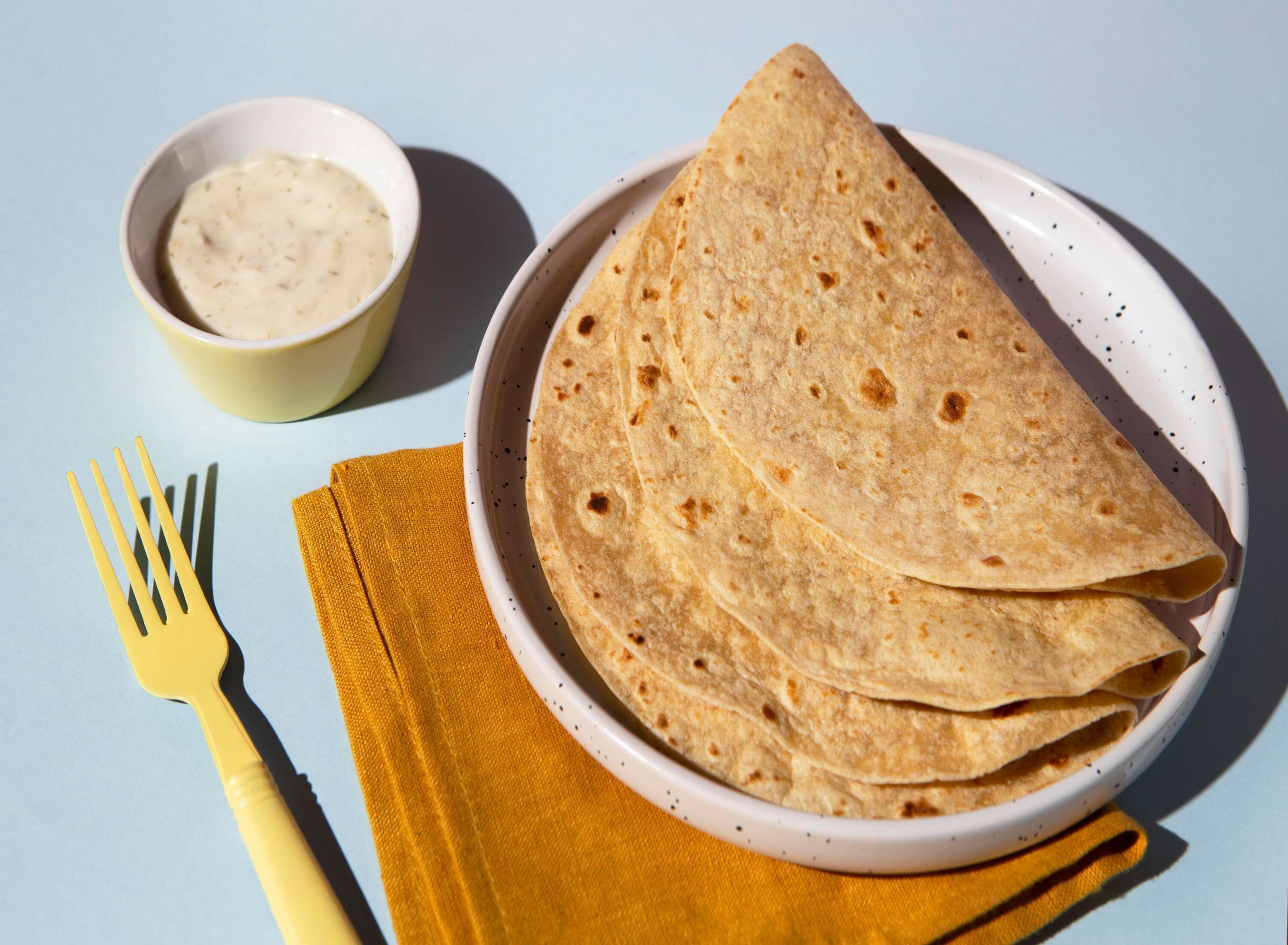 A plate of folded tortillas with a small bowl of sauce and a yellow napkin.