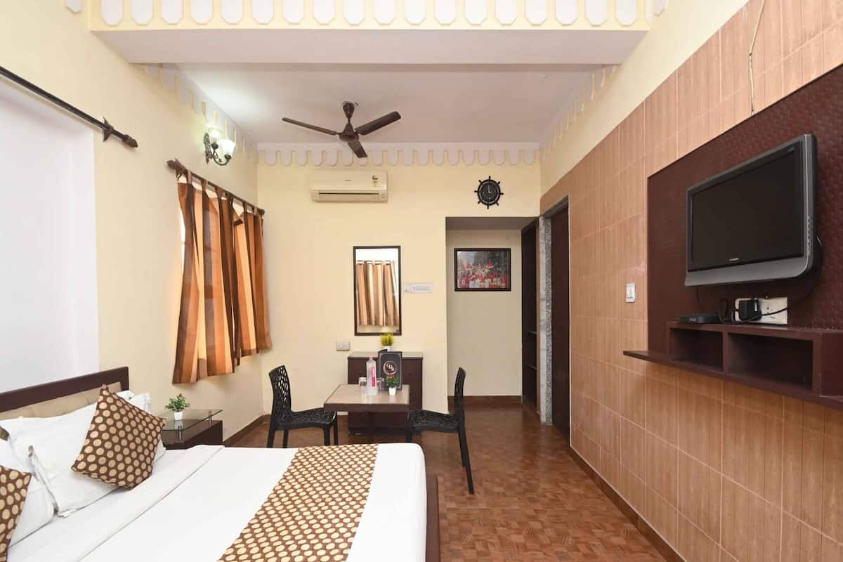 A hotel room with a bed, a desk, a chair, a television, and an air conditioning unit.