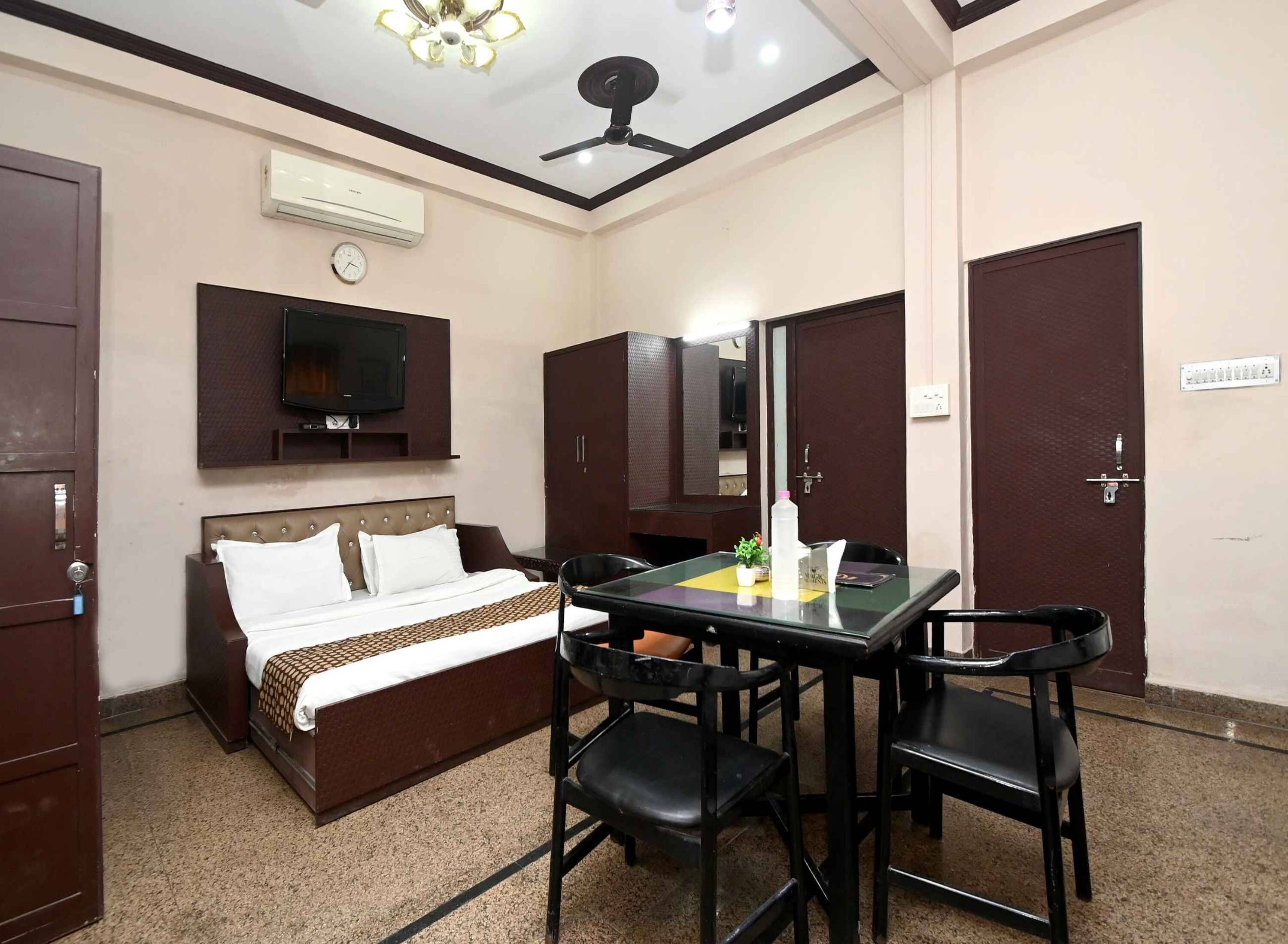 Una habitación de hotel con cama, escritorio con sillas, televisión, armario y ventilador de techo.
