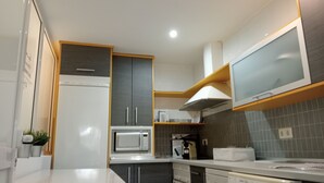 Une cuisine moderne avec des meubles gris, un plan de travail blanc, un four à micro-ondes, une machine à café et un lave-linge.