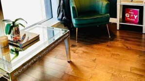 A modern room with a green armchair, a glass table with books and a candle, a lamp, and a shelf with a book titled "Fire Givy Island". - New Luxury apt,Javits Center,NYC (New York)