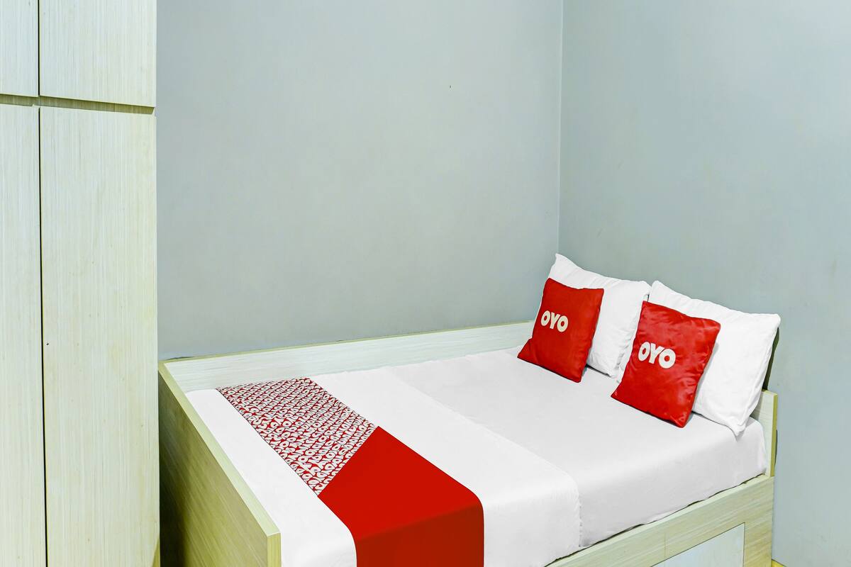 A single bed with a white and red bedspread, two red pillows with white text, and a white headboard.