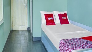 Ein Hotelzimmer mit einem Bett, zwei rote Kissen mit dem Schriftzug "OYO", einem weißen Bettbezug und einer roten und weißen Decke.