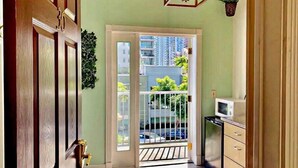 Un pasillo con una puerta de madera, una puerta de vidrio con marco blanco que da a un balcón, una lámpara colgante y un microondas sobre una encimera.