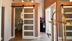 Un pasillo con una puerta corredera que da a un baño, una zona de cocina y una estructura metálica decorativa.