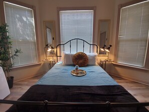 A bedroom with a bed, bedside lamps, a bedside table, and a window with blinds. - Somerset  (San Diego)