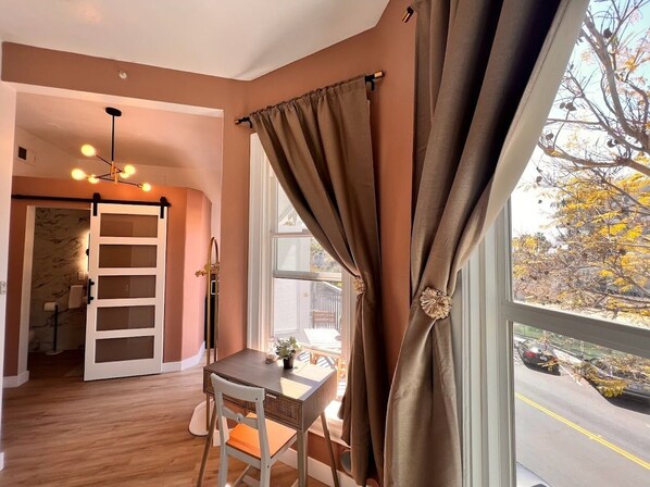 A room with a dining table, a chair, a window with curtains, and a door leading to another room. - Somerset  (San Diego)