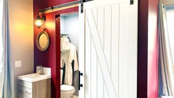 Un baño con inodoro blanco, tocador de madera, un perchero con bata y una puerta corredera tipo granero.