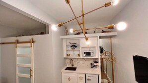 Cocina compacta con armarios blancos, microondas y lavamanos. Una escalera conduce a un área de almacenamiento en altura.