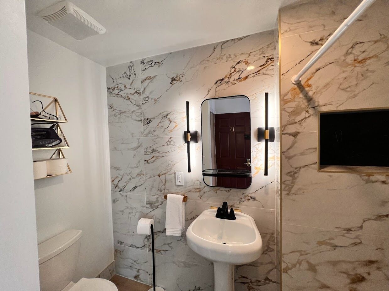 Une salle de bain avec un mur en marbre, un lavabo blanc, un miroir et un porte-serviettes.