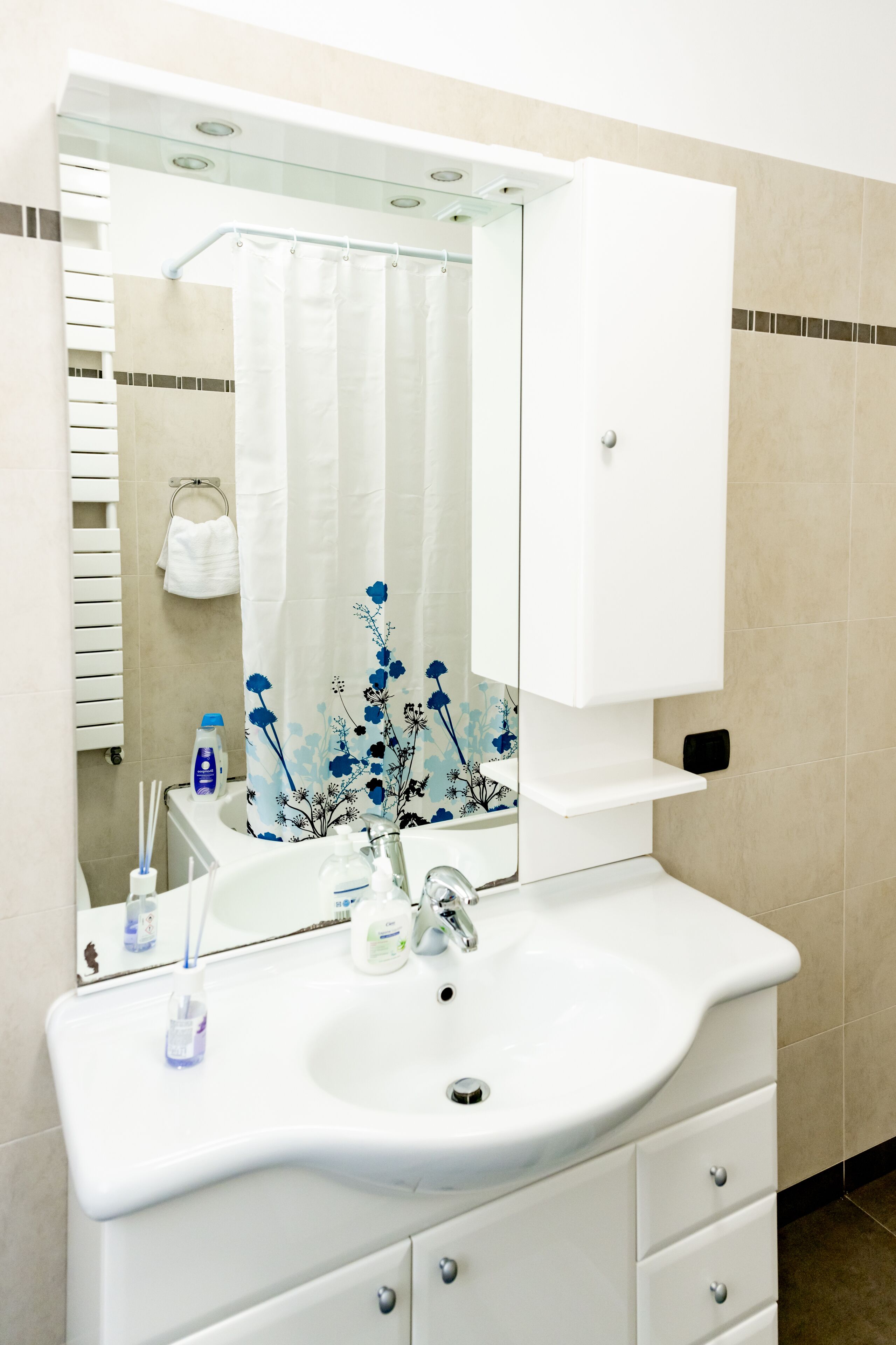 A bathroom with a white sink, mirror, and cabinet. There is a shower curtain with floral patterns and a towel rack with a towel.