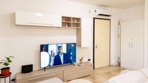 Una sala de estar moderna con un televisor de pantalla plana, un sofá, una mesa de centro, una planta en maceta y un mueble con estantes.