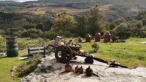 Paisagem rural com um trator antigo e equipamentos agrícolas, cercada por campos verdes e colinas ao longe.