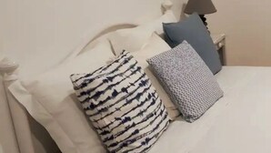 Uma cama com roupa de cama branca, um travesseiro listrado e um travesseiro estampado.