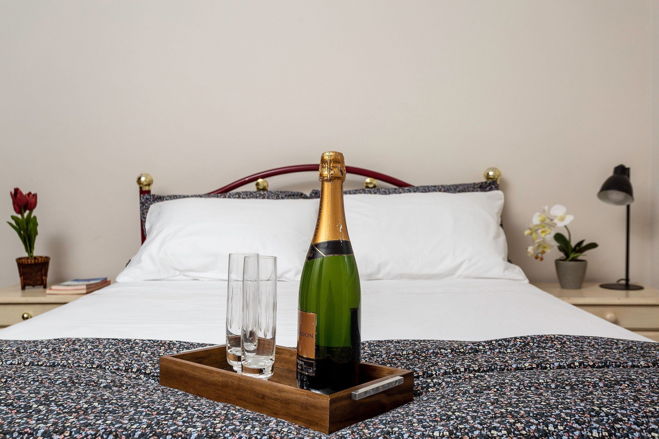A bed with a wooden tray holding a bottle of champagne and two glasses.