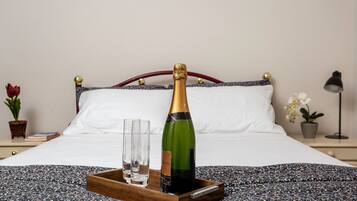A bed with a wooden tray holding a bottle of champagne and two glasses.