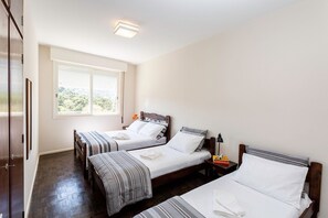 Une chambre d’hôtel avec deux lits simples, une armoire, une fenêtre donnant sur un paysage agréable et une table de chevet avec une lampe.