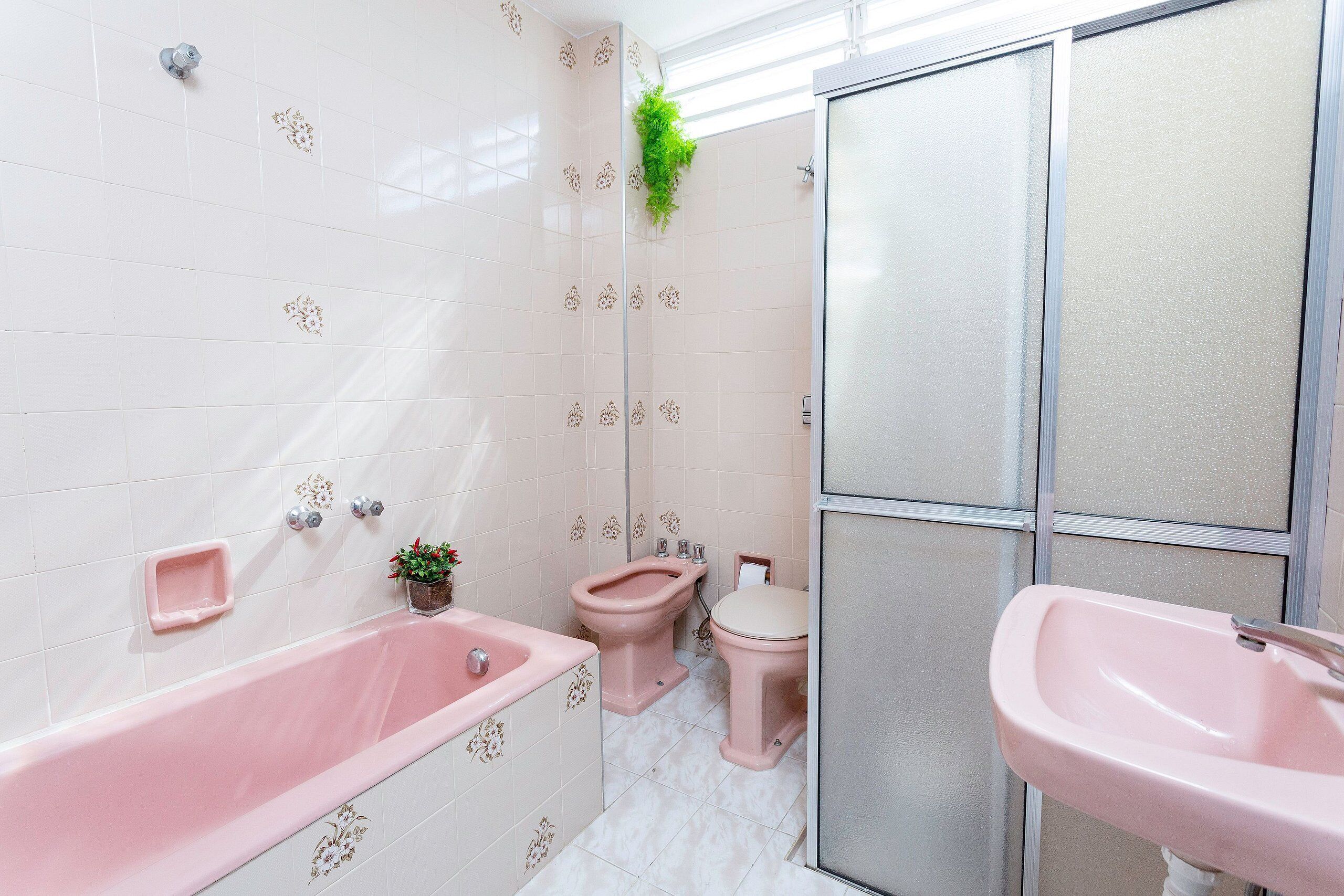Un baño con una bañera rosa, un inodoro y un lavabo.