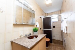 Une salle de bain avec un lavabo doté d’un plan de travail en granit, un miroir, une plante en pot, des toilettes et un espace douche.