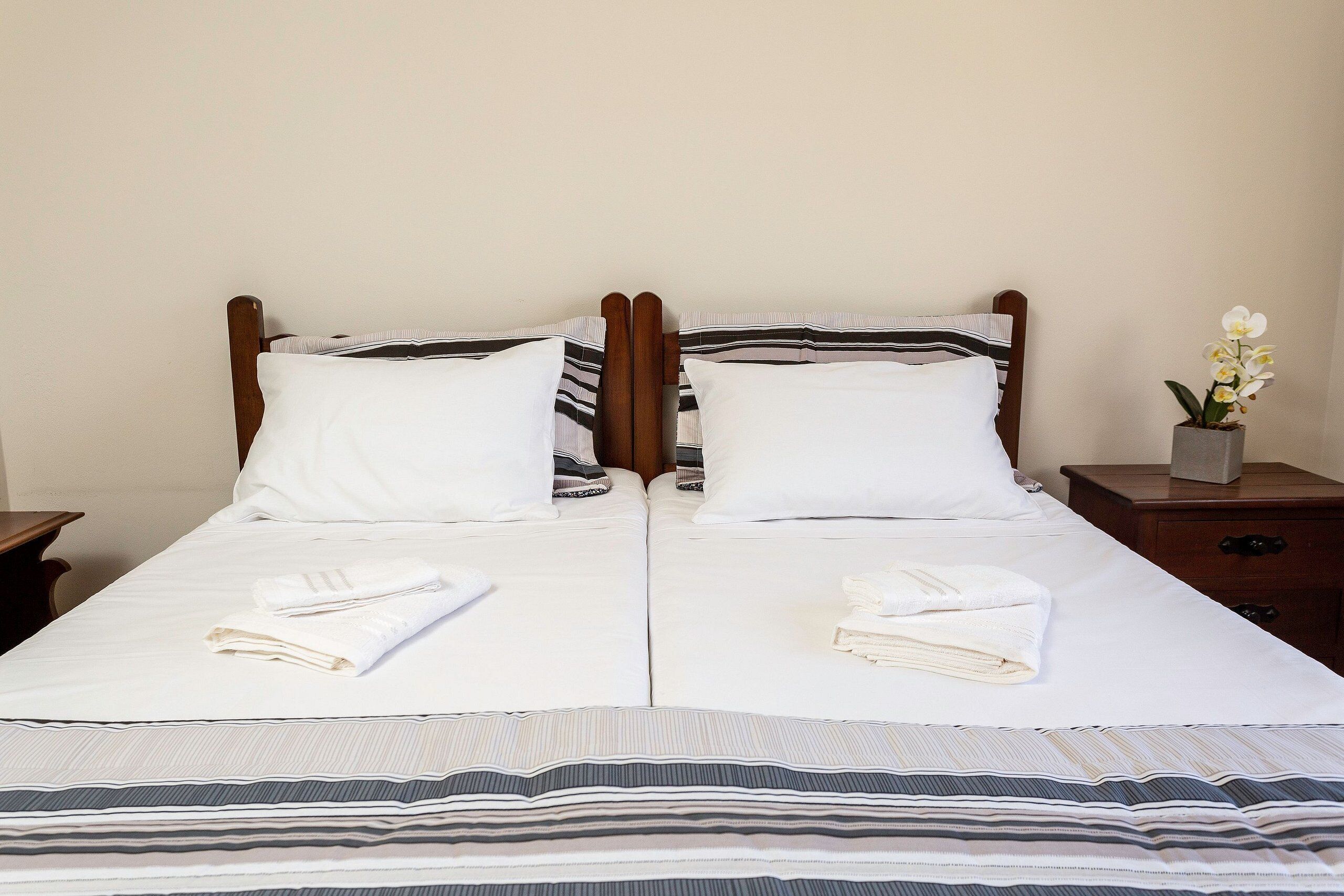 A double bed with white linens, striped pillows, and folded towels.