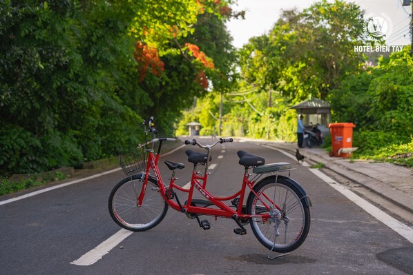 A red bicycle parked on a road with greenery on both sides. - Bien Tay hotel (Ha Tien)