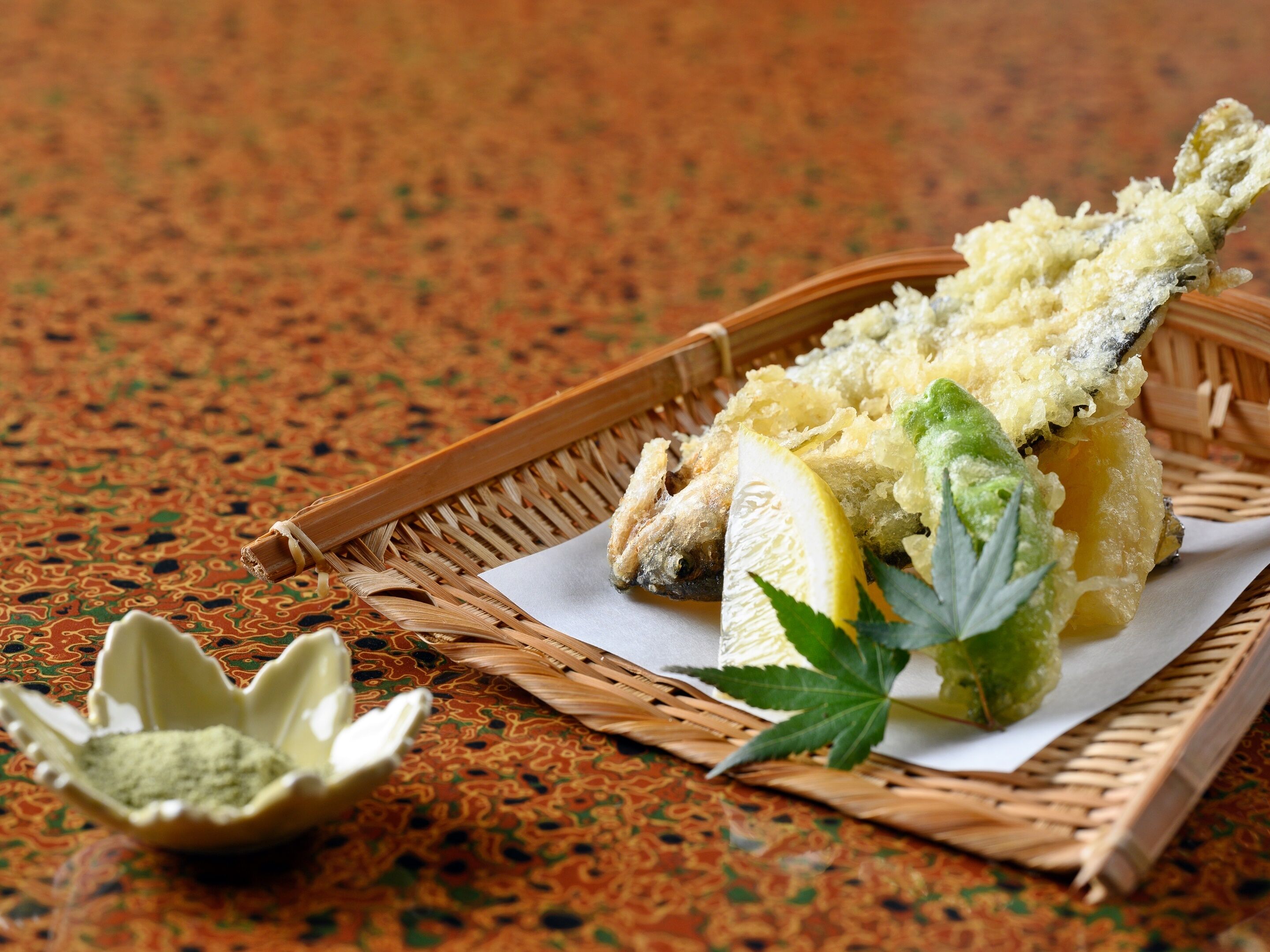 A basket containing a fried fish, lemon slices, and a small bowl of green seasoning.