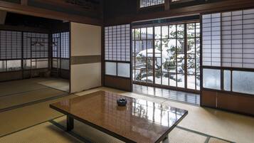 A traditional Japanese room with tatami flooring, a low table, sliding doors, and large windows with a view of a snowy garden.