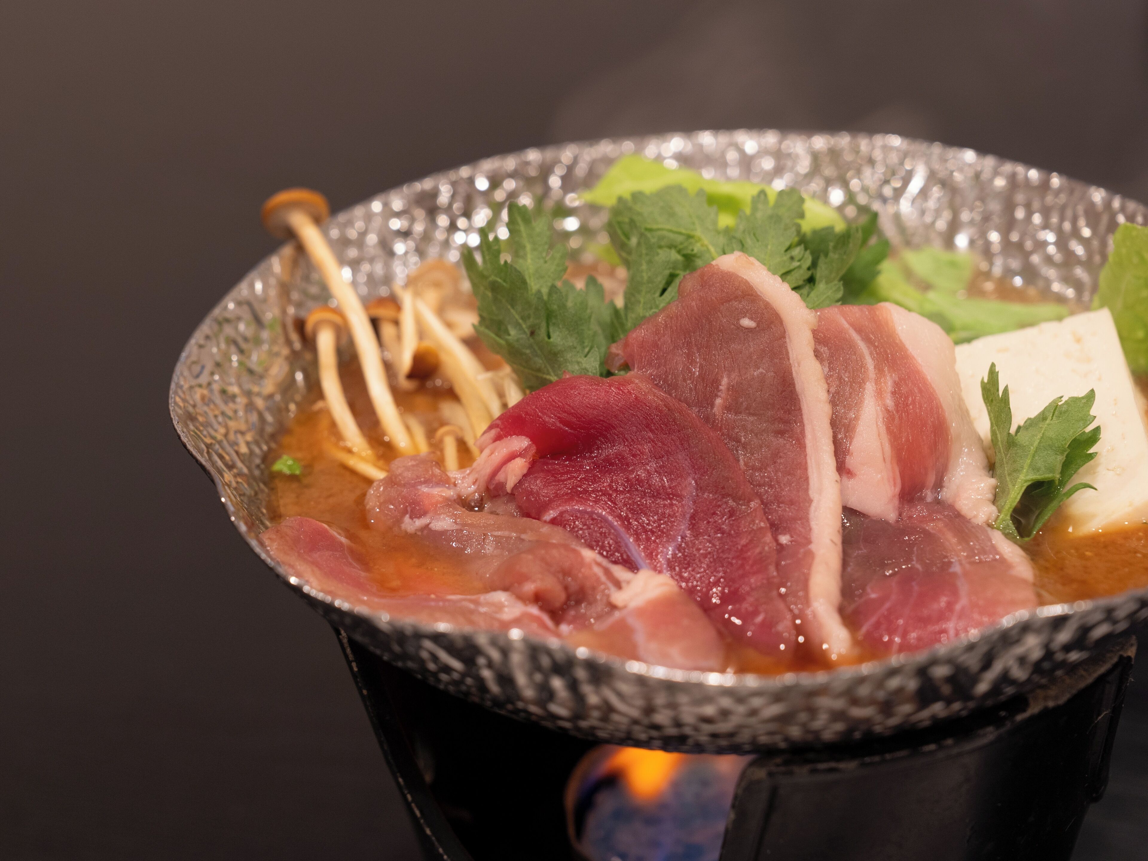 A bowl of hot broth with various ingredients including meat and vegetables.