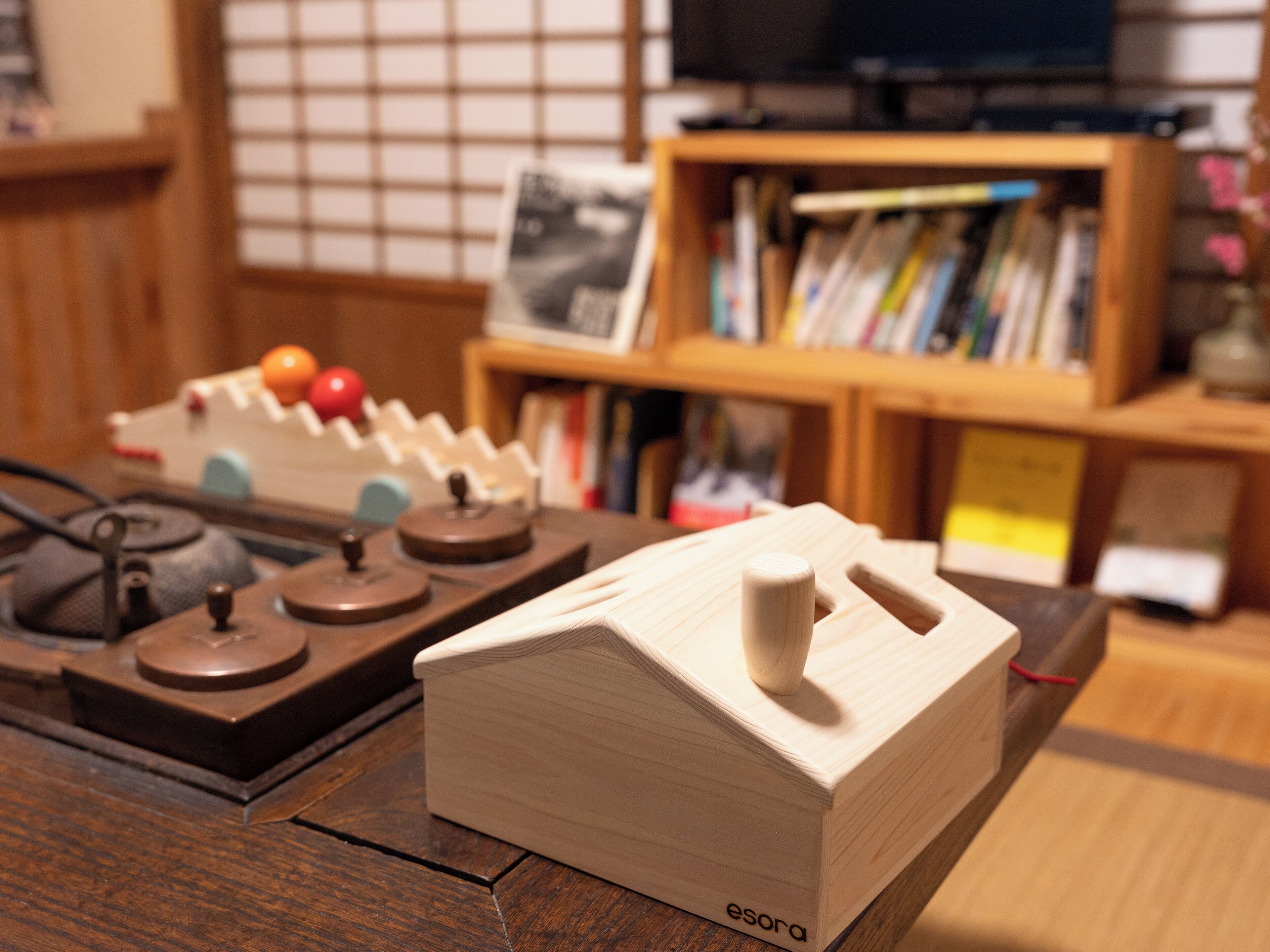 Un escritorio de madera con un pequeño modelo de casa de madera, una radio antigua y una estantería al fondo.
