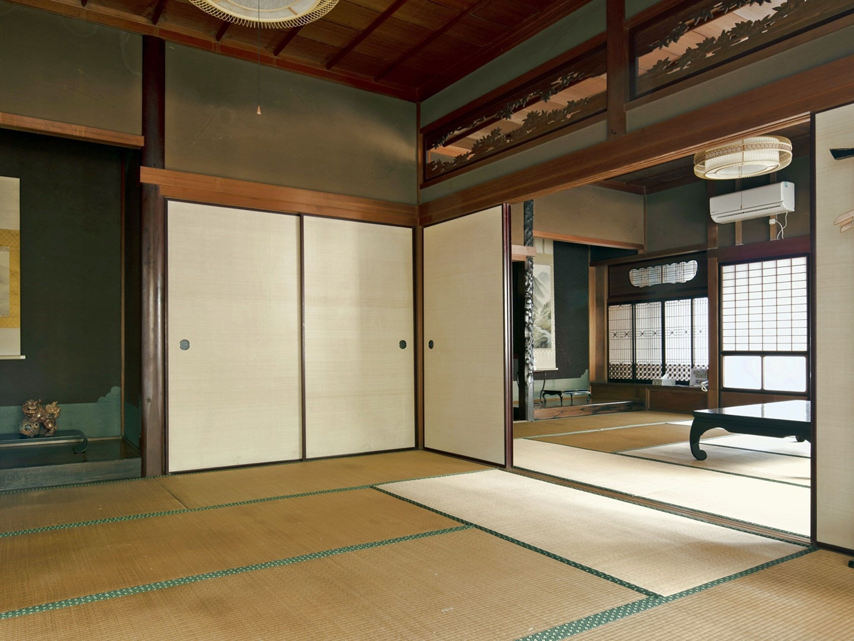 A traditional Japanese room with tatami flooring, sliding doors, and a view of a garden through a window.