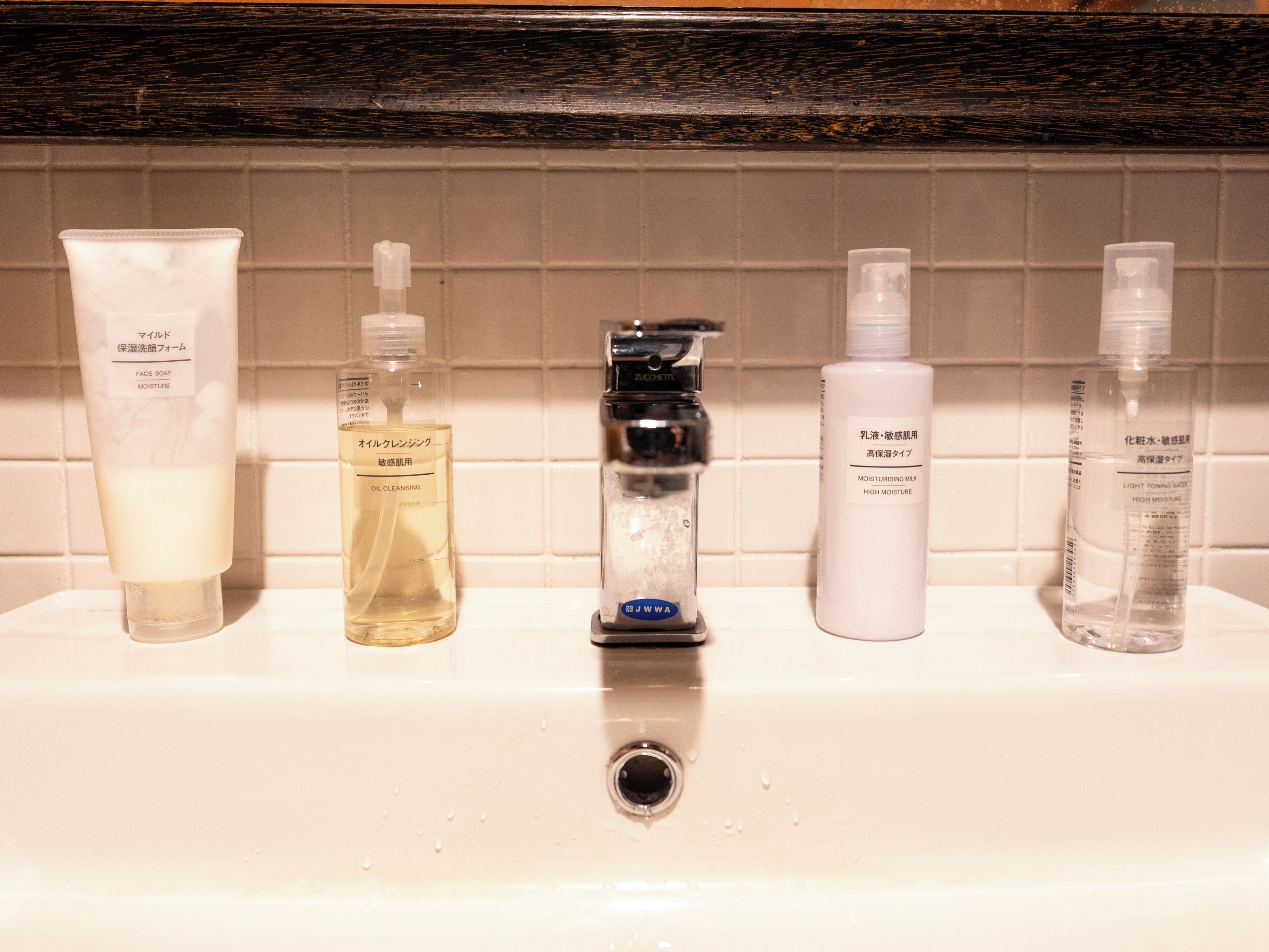 A bathroom sink with five bottles of skincare products.