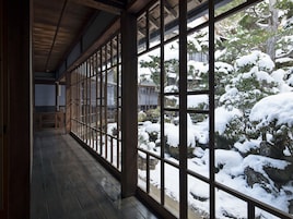 Una habitación tradicional japonesa con suelo de tatami, puertas correderas y vistas a un jardín cubierto de nieve.