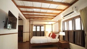 Ein Bett mit Baldachin, dessen Gestell aus Holz besteht, ein Nachttisch mit Lampe sowie ein großes Fenster mit Vorhängen.