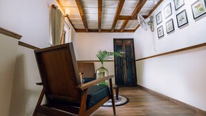 Ein Holzstuhl mit Kissen, eine Vase mit Pflanze und gerahmte Pflanzenbilder an der Wand.