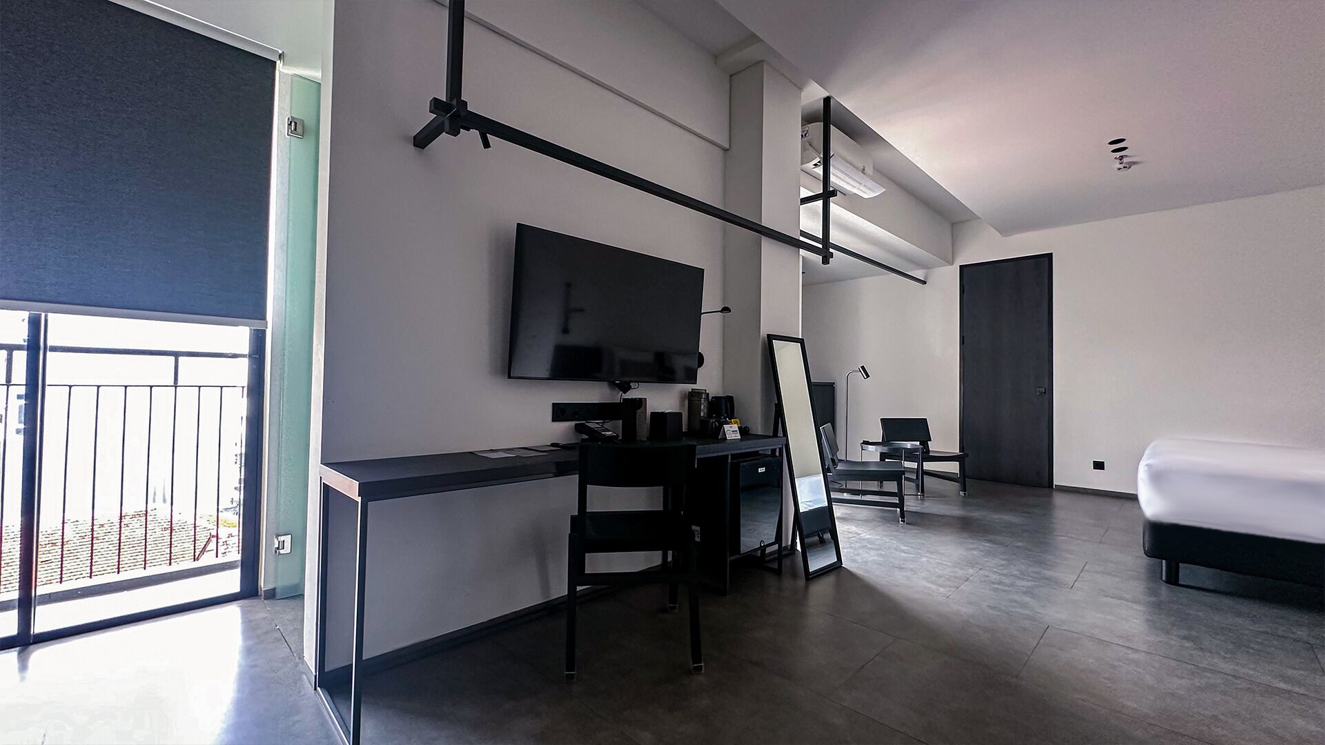 A modern hotel room with a desk, chairs, a bed, and a TV.