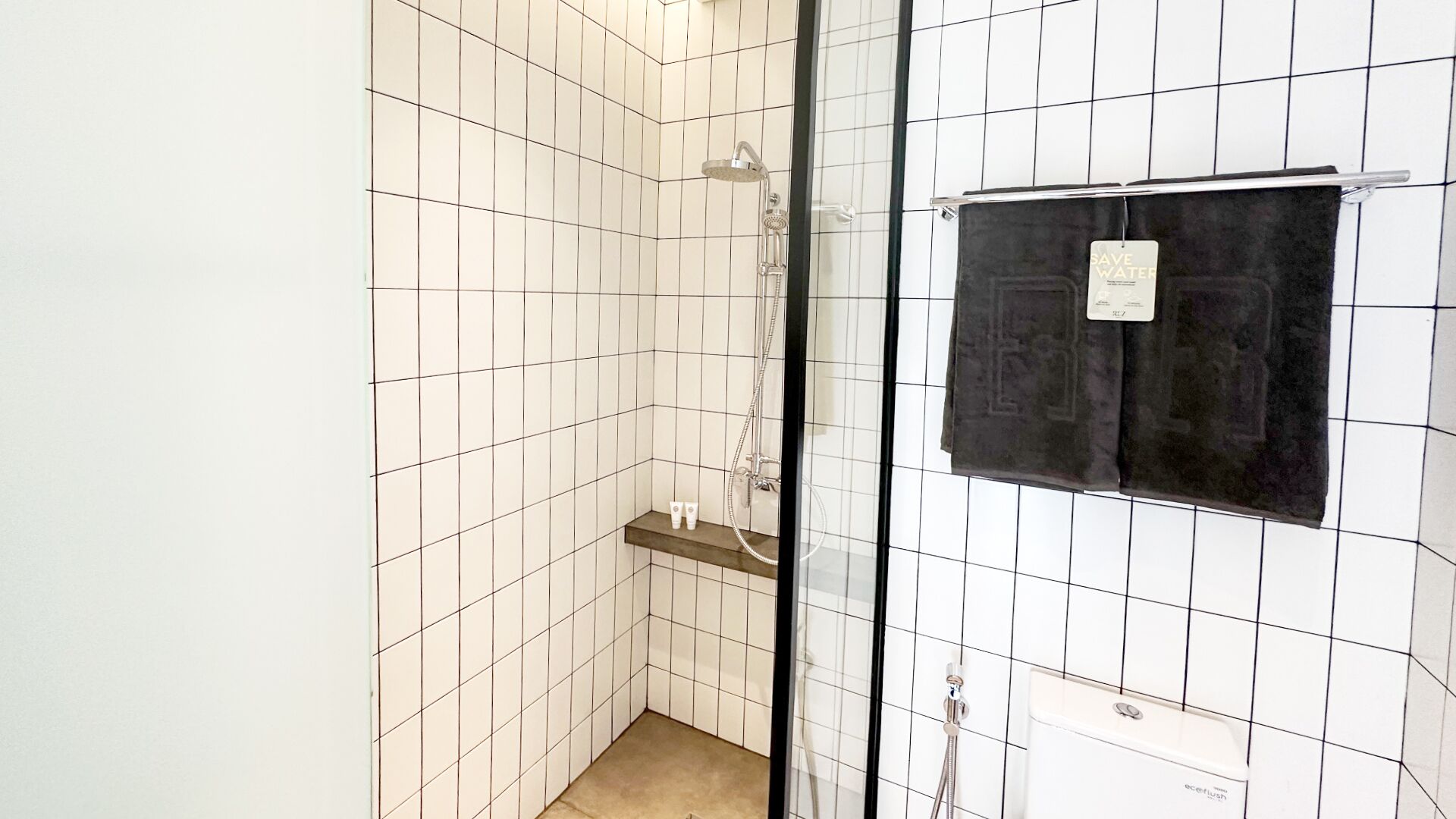 A small, tiled bathroom with a shower, a towel rack, and a shelf with toiletries.